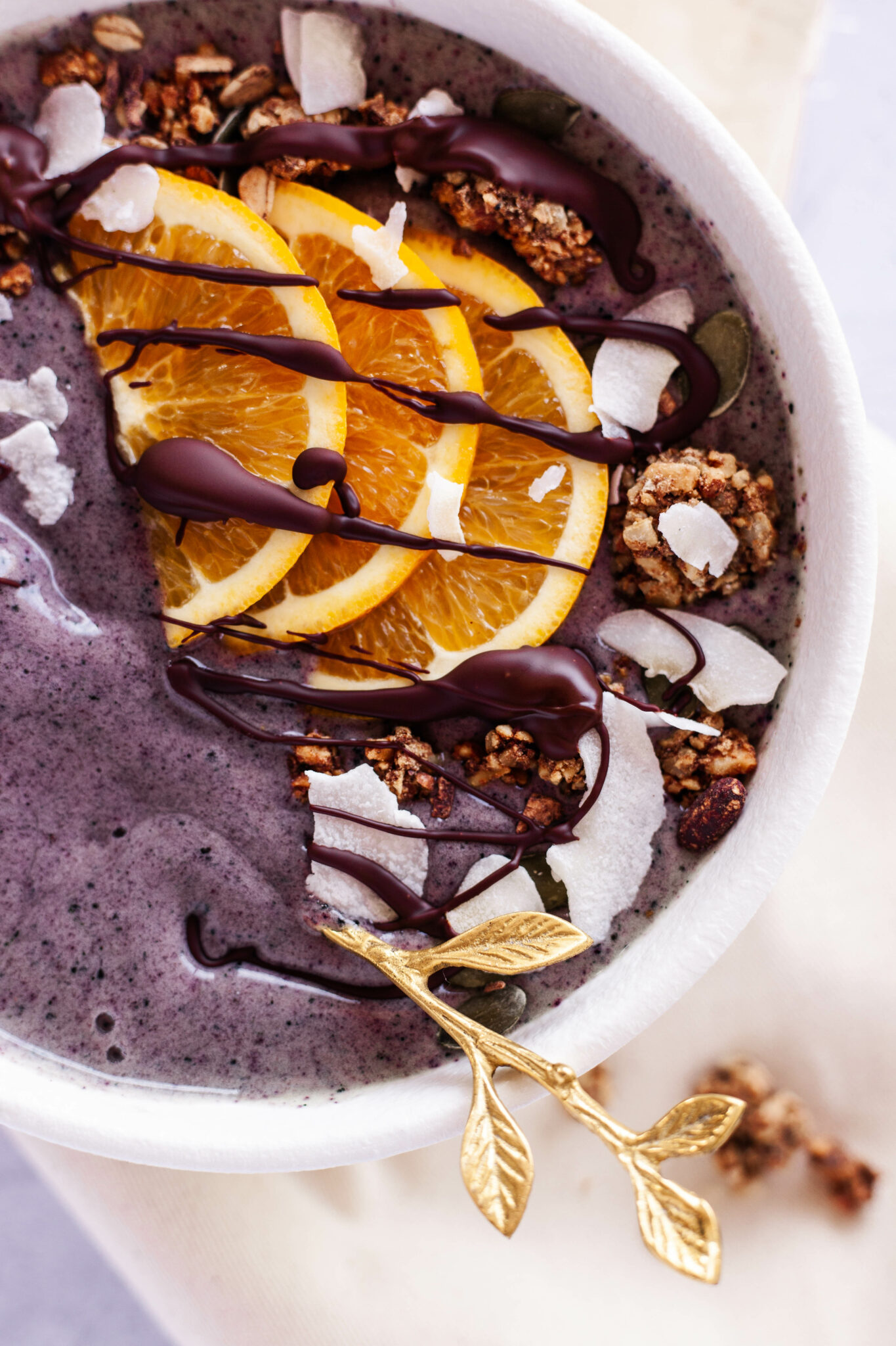 Purple smoothie bowl with chocolate drizzle and sliced oranges